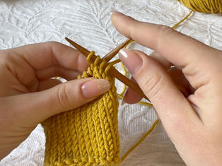 Hands knitting with yellow yarn and wooden needles on a white textured fabric background. Close-up, focused, and calm setting.