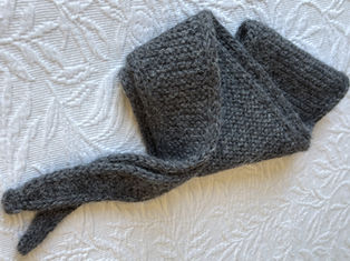 Grey knitted wool Sophie Scarf, by PetiteKnit, on a white quilted bedspread.