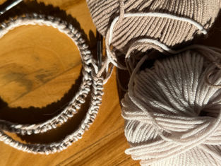 Two balls of yarn, one beige and one white, with a circular needle that contains a completed long-tail cast on, placed on a wooden surface. Sunlight casts shadows, creating a cozy mood.
