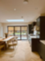 Modern kitchen with wooden table, chairs and glass doors looking outside.