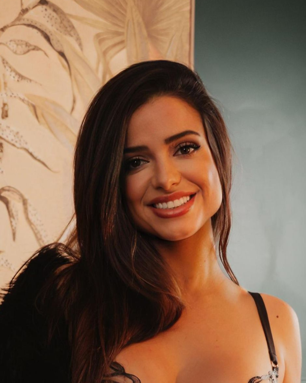 Smiling woman in lingerie posing with black feathery wings in background.