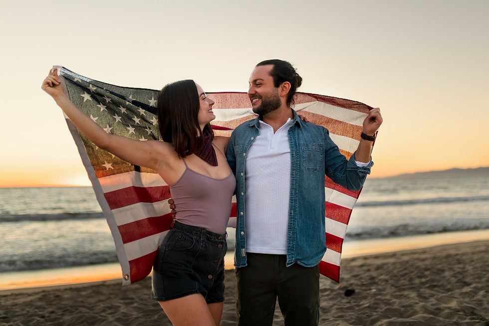 Couple holding American flag with sunset background on the beach together