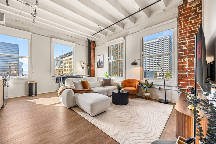 Modern furnished apartment living room with large windows and city view.