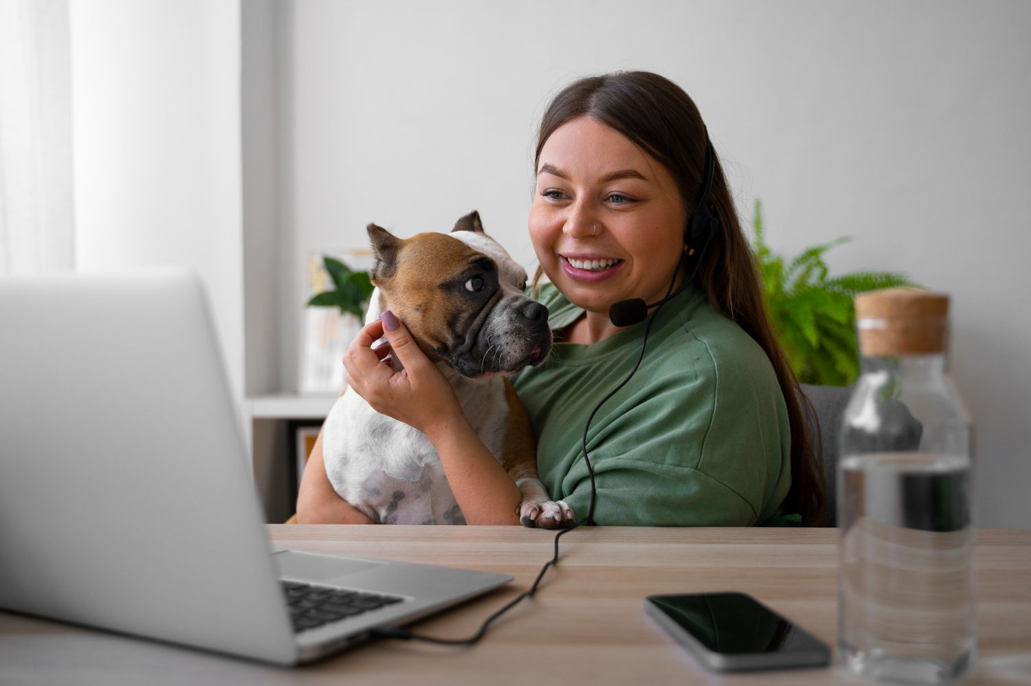 Smiling woman with bulldog on lap making a video call with headset.