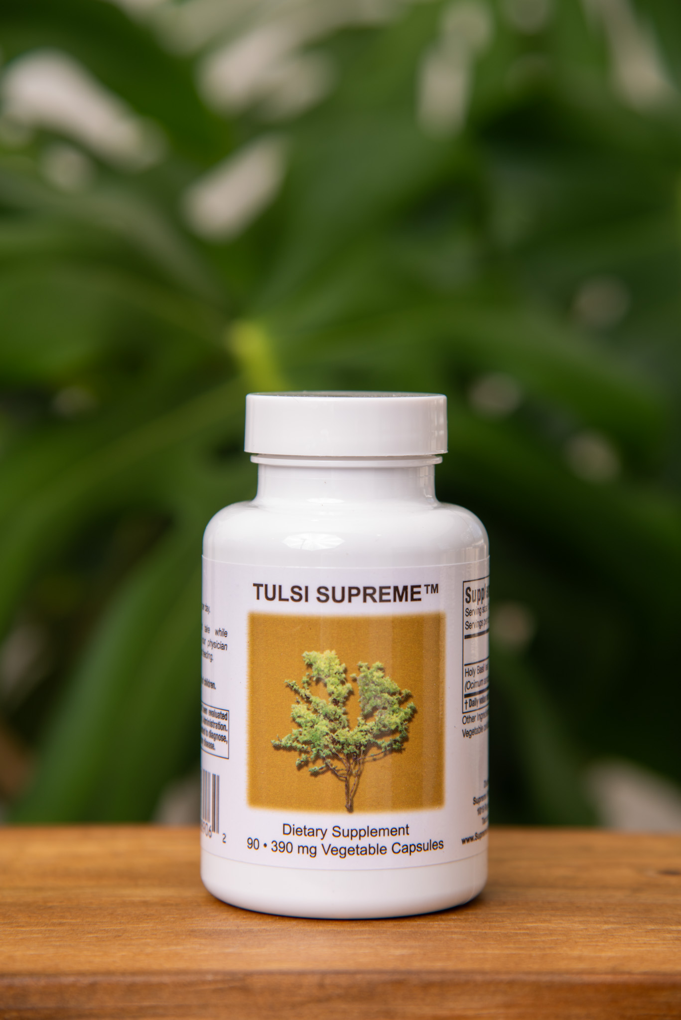 Tulsi Supreme holy basil bottle on a wooden surface against green foliage