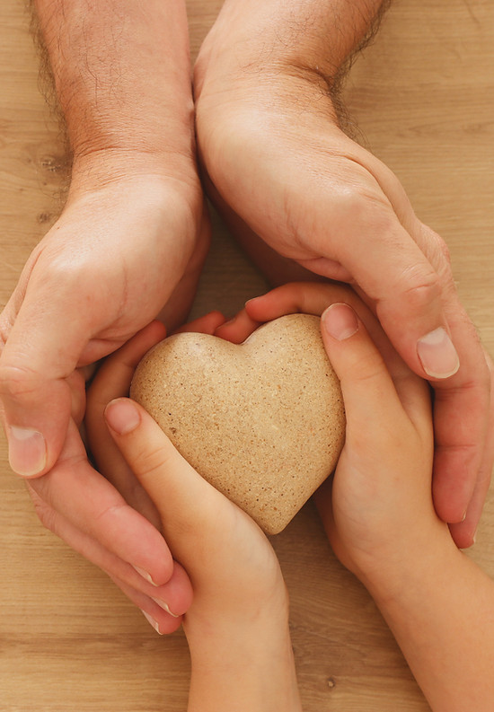 Le mani di un adulto tengono delicatamente le mani di un bambino, simboleggiando il sostegno e la connessione nella genitorialità