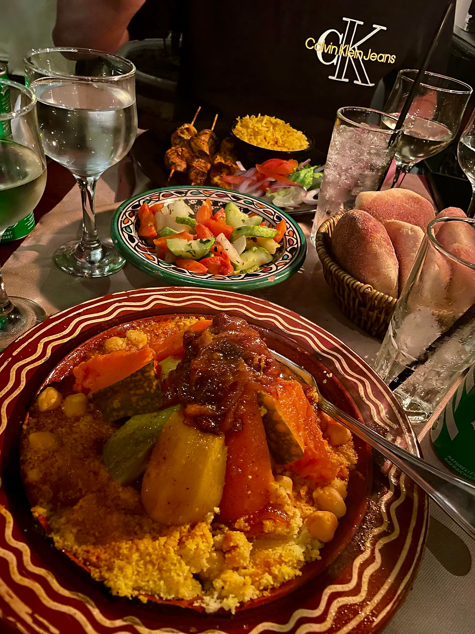 A plate of couscous with vegetables and another plate with chicken skewers on it