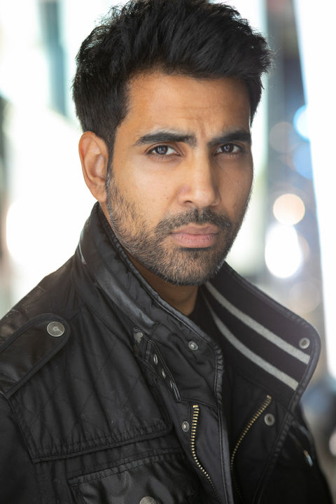 A Male actor in a black leather jacket, he has a serious expression, with ablurred background