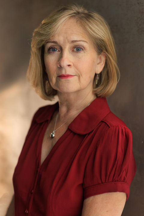 A Mature actor in a deep red blouse with complimneting red lipstick, she has an elegant expression under warm professional lighting