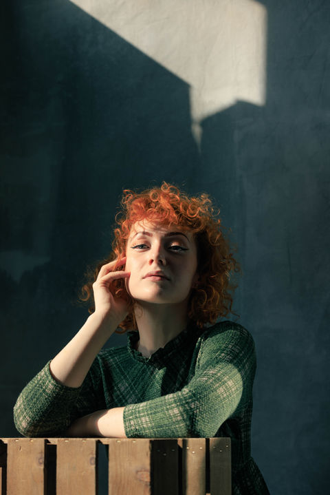 A lady with curly red hair in shadowed lighting. It is an artistic studio portrait