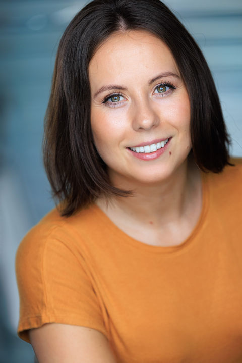 An actor with short brown hair in orange top the style is a relaxed and approachable studio portrait