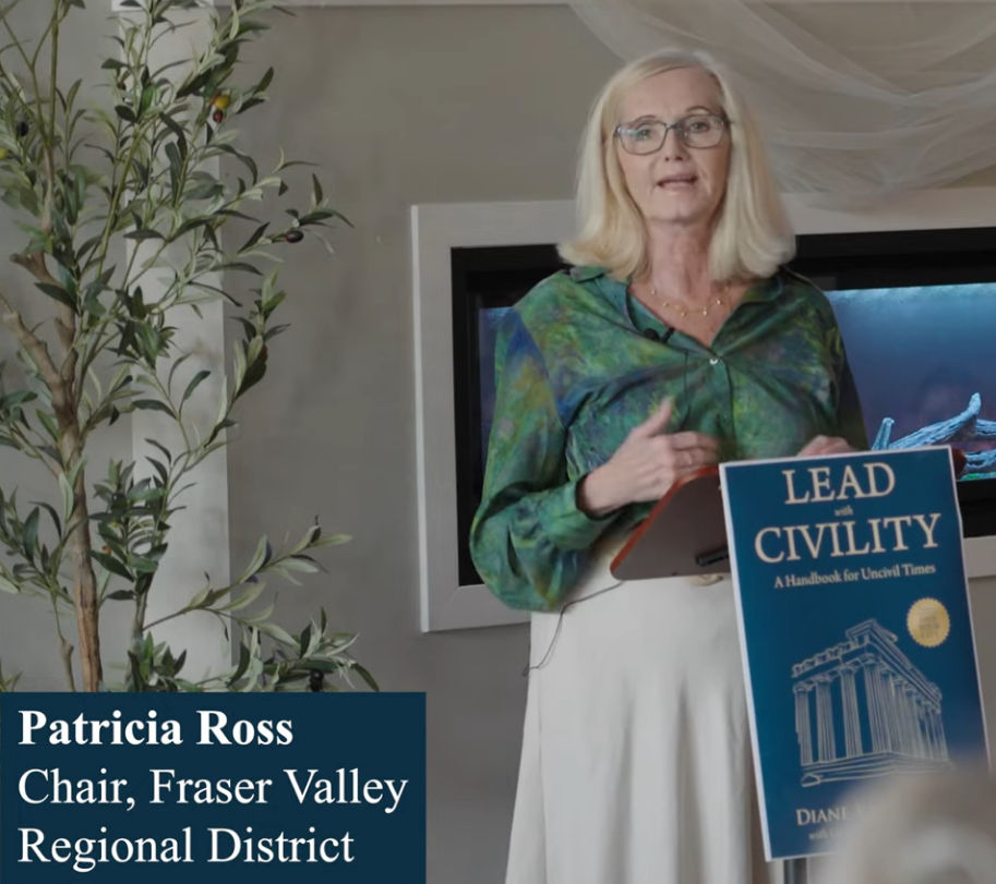 Woman with glasses speaking, holding a book titled "Lead with Civility." Background shows a plant and a screen. Calm, professional setting. Patricia Ross.