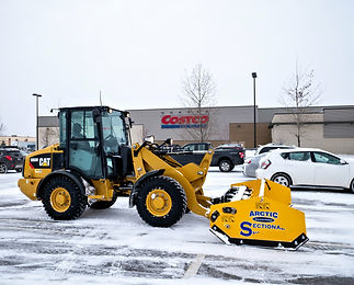 Yellow CAT front end loader machine clearing snow for a commercial building parking lot with an arctic sectional plow blade