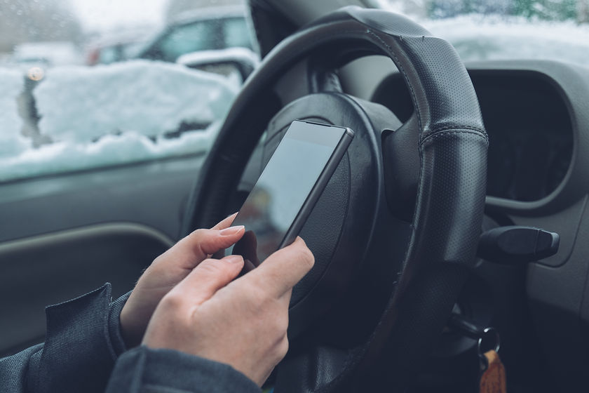 Texting on phone in a parked car while snow is falling outside.