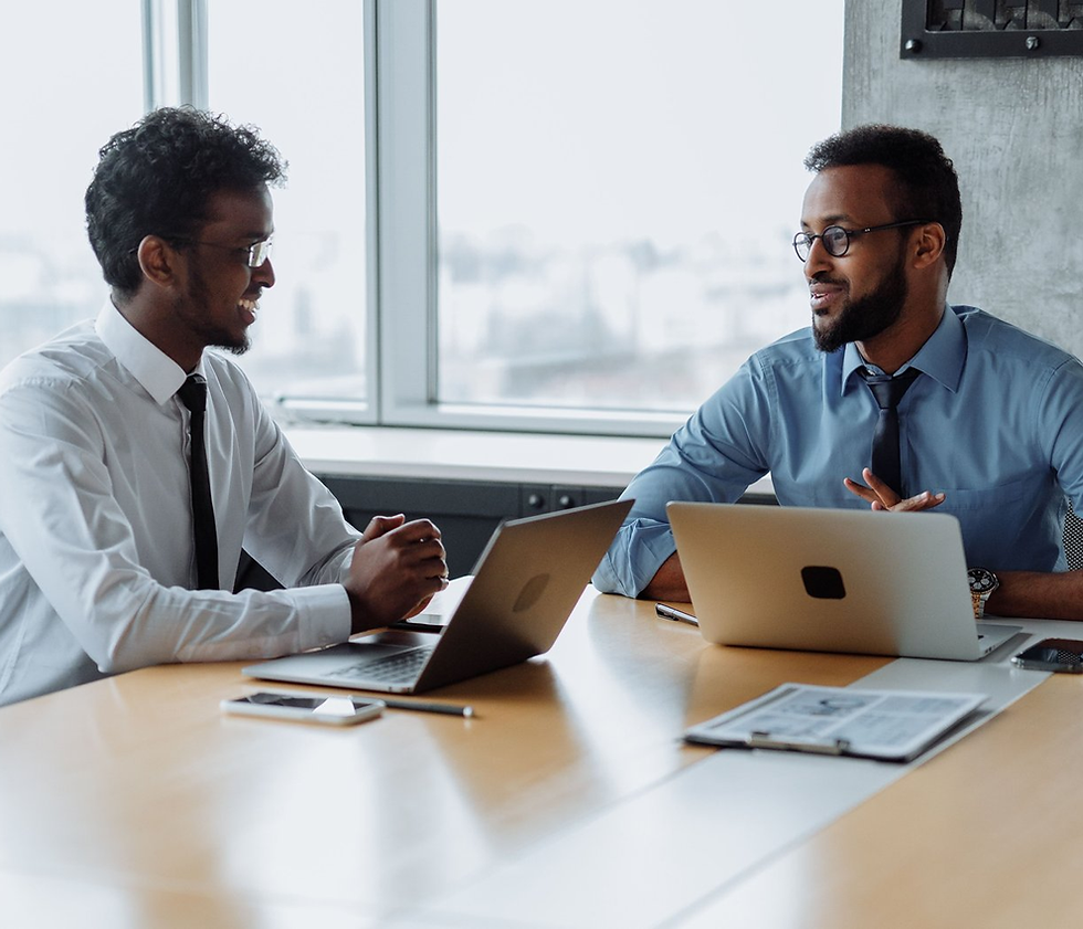 Two professionals sitting at a conference table with laptops in a bright office.