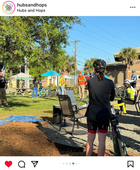 Nora examines photos in the background while cyclists wait for the race to start.