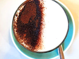 A cappuccino in a teal cup with chocolate on top. 