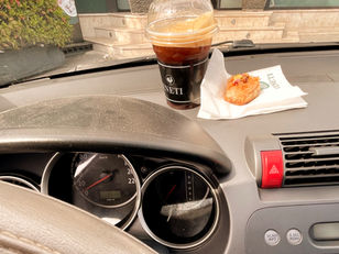 An iced coffee in a plastic takeaway cup and a pastry on a serviette resting on the dashboard of a car. 