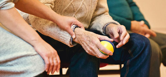 Physical therapist assisting a senior with strengthening his hand.