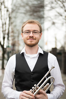 Jesse Baker smiling outside in Atlanta while holding his trumpet