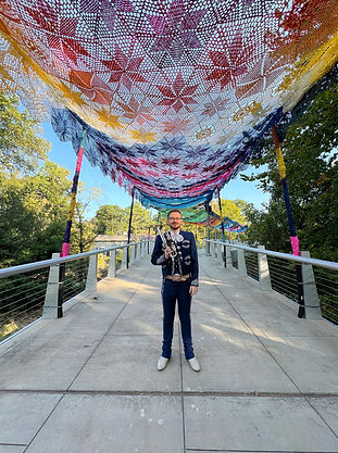 Jesse Baker wearing his mariachi outfit while holding his trumpet under a mexican tapestry