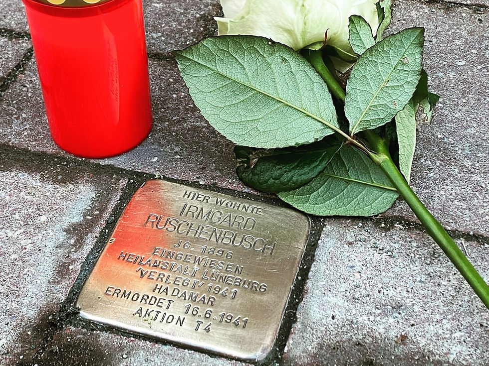 Ein Stolpersten mit Kerze und weisser Rose