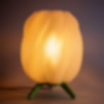 Lampa stołowa z falistym, półprzezroczystym kloszem, na miętowych nożkach, widok od przodu, włączona.