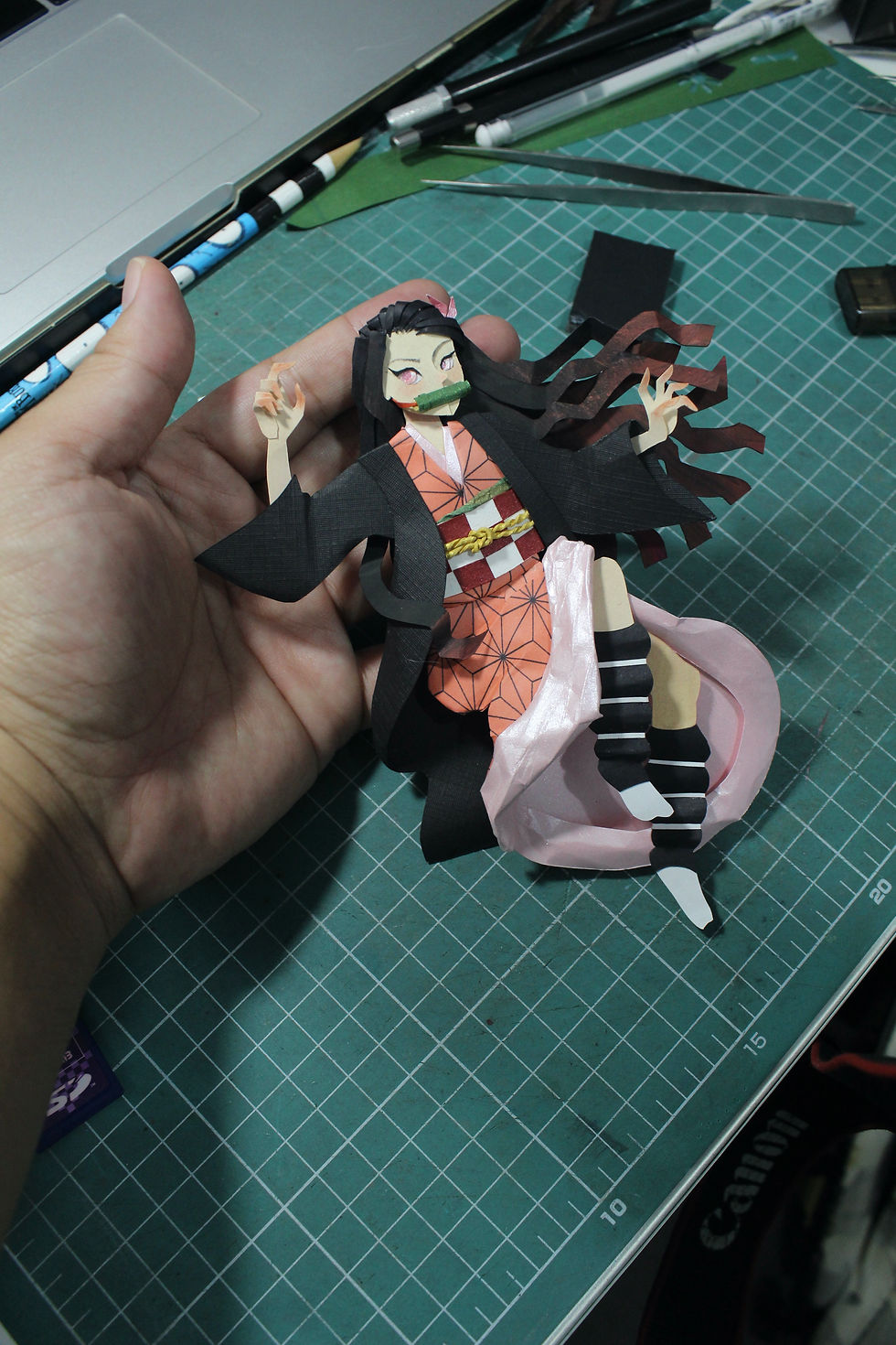 Nezuko Kamado em arte de papel, na mão de uma pessoa.