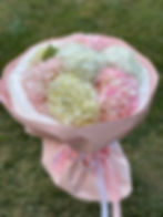 An elegant bouquet of hydrangeas in pastel shades of white and pink, wrapped in delicate pink paper with satin ribbons.