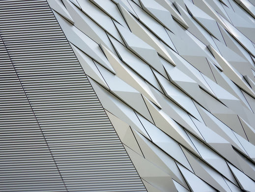 Abstract architectural detail with vertical lines and geometric patterns in silver and gray tones, creating a modern, textured surface.