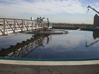 Workers on a bridge over a large water treatment clarifier tank.