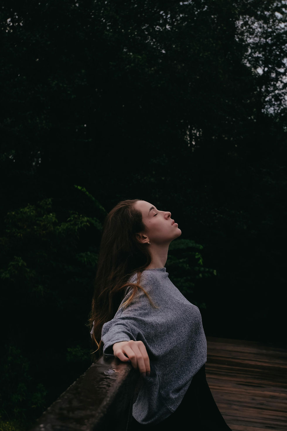 Young woman looking up peacefully, leaning on a railing outdoors.