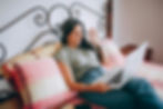 Smiling woman on bed waving during video call on laptop