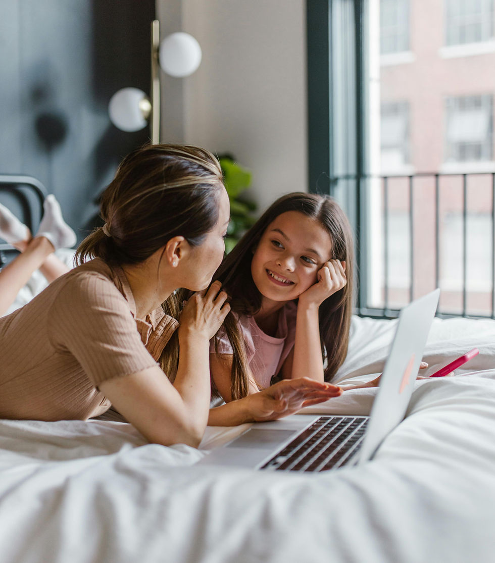 A mother and daughter enjoy quality time together, smiling and conversing while looking at a laptop in a cozy room.