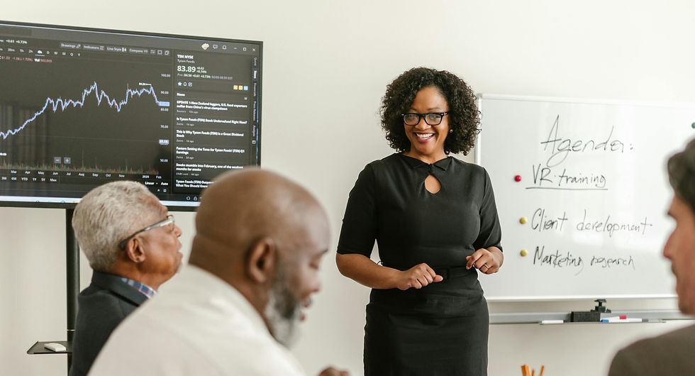 Woman presents to colleagues, graph on screen, agenda on whiteboard.