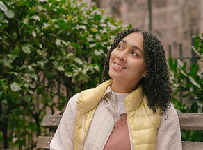 Young woman with curly hair smiles on park bench