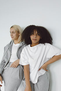 Two young women, blonde and dark-haired, wearing white shirts and grey sweatsuits.