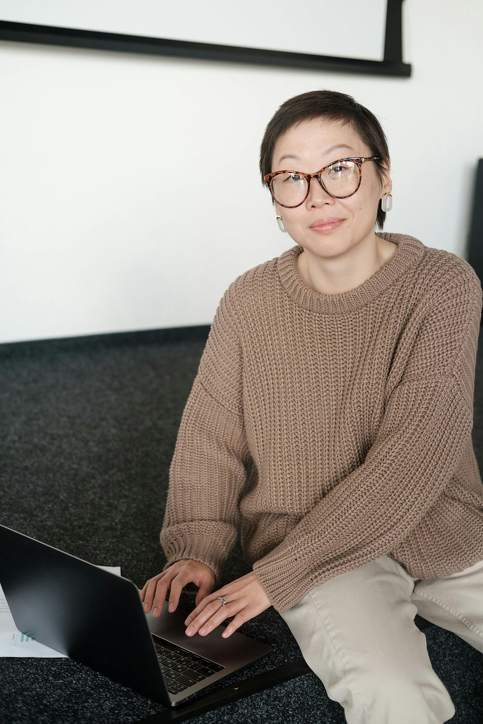 Asian woman in glasses smiling, working on laptop on a couch.
