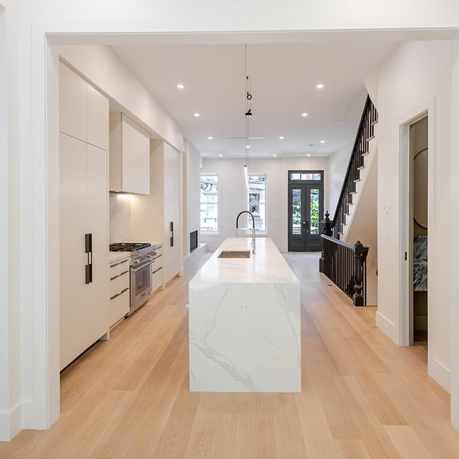 Long view through the open main level toward the white kitchen island, staircase and rear windows