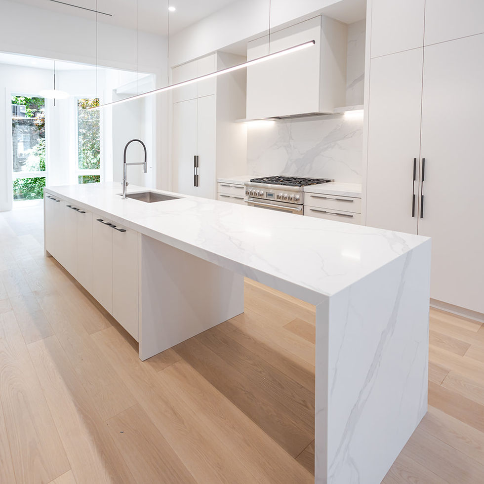 Custom white kitchen with a waterfall-edge stone island, integrated appliances and linear pendant lighting