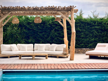 Pergola en bois flotté installée près d’une piscine, avec luminaires suspendus, canapé extérieur et végétation en fond.