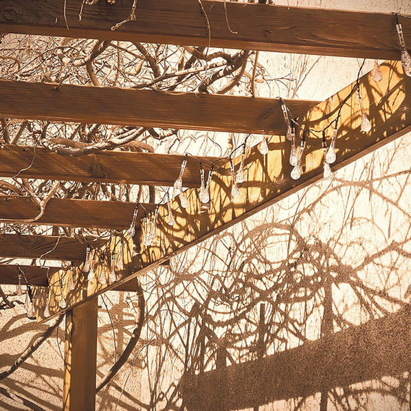 Structure de pergola en bois avec ombres de glycine dans une cour intérieure à Sainte-Florine.