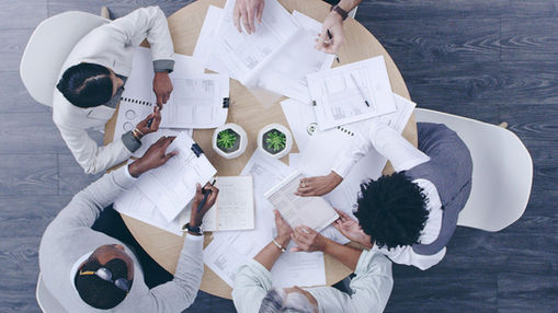 Overhead view of business team members seated at a round table working on separate documents with minimal interaction.