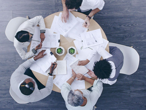 Overhead view of business team members seated at a round table working on separate documents with minimal interaction.
