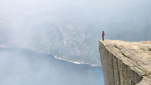 Person standing on a mountain peak at sunrise, looking into a misty, uncertain landscape—symbolising leadership under uncertainty.