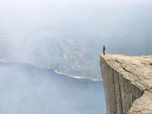 Person standing on a mountain peak at sunrise, looking into a misty, uncertain landscape—symbolising leadership under uncertainty.