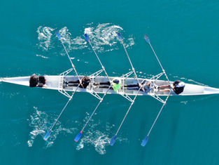 Rowing team moving in unison on calm water, symbolising alignment and coordinated execution.