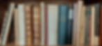Books with ornate covers and varied colors stand upright on a wooden shelf. Visible titles include "Wapen boek van Europa" and "Aventures Galantes".