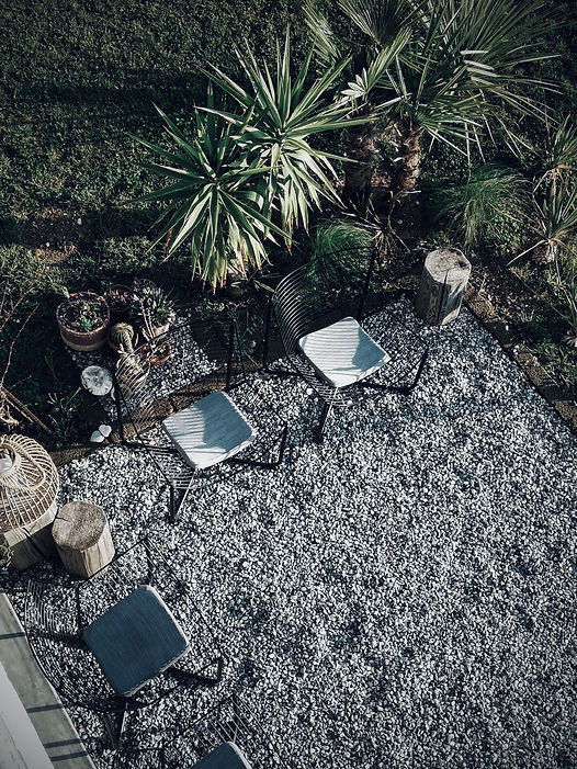About Bed & Breakfast IL PAJO.Outside gravelled terrace and modern seating area with black iron lounge chairs and gray cushions. A bamboo candle holder and small tree trunk tables as decoration.