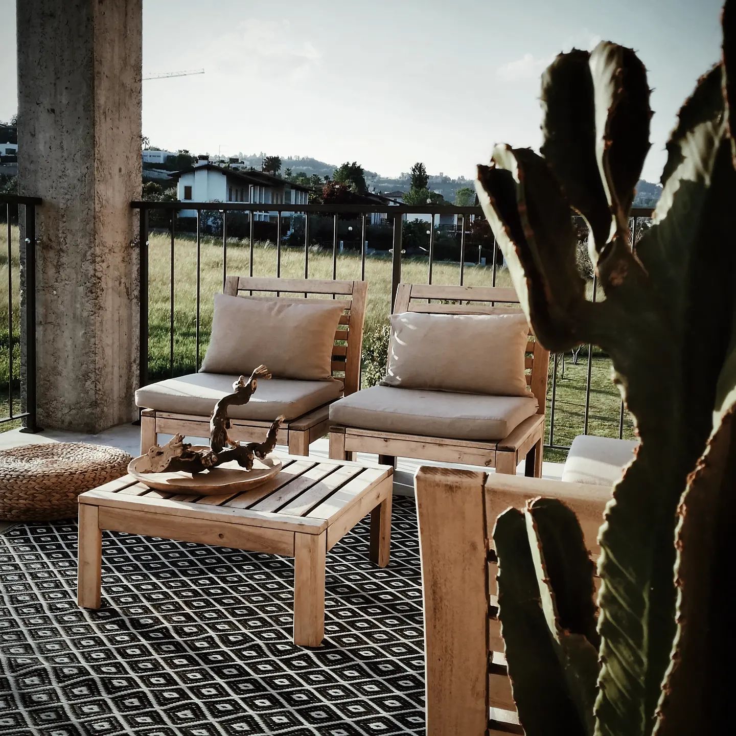 Bed & Breakfast Il Pajo. Outdoor terrace with wooden furniture with natural colors, boho deco, concreet and cactus in the front, surrounded by greenery.